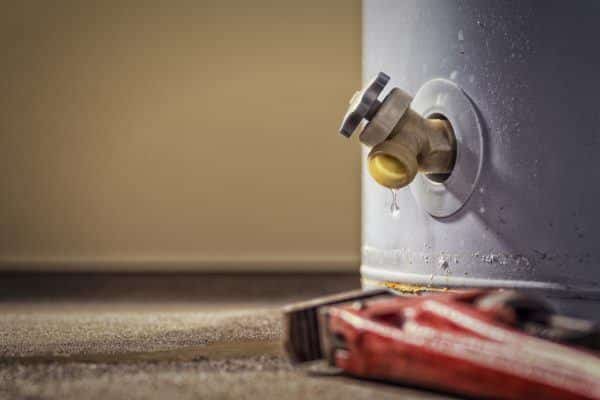 Close-up of a valve on a water heater Colorado with a small leak, as a drop of water hangs from the spout. A red pipe wrench lies on the floor—reminding you the best time to replace water heater might be now. | High 5 Plumbing, Heating & Cooling