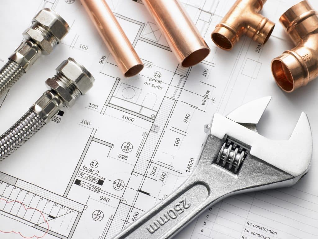 Plumbing tools, copper pipes, flexible hoses, and fittings are arranged on top of architectural blueprints—perfect for a home repiping project. A large adjustable wrench is also visible in the foreground. | High 5 Plumbing, Heating & Cooling