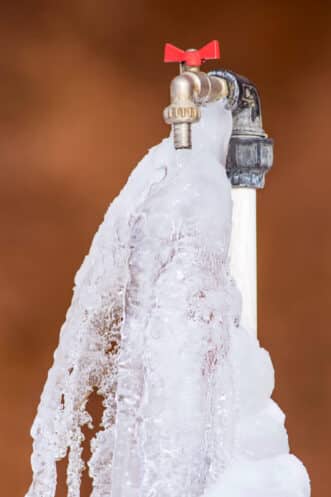 An outdoor water faucet with a red handle is covered in ice, showing frozen water flowing from the spout—an example of outdoor faucet freezing and a reminder to protect outdoor faucets in cold temperatures. | High 5 Plumbing, Heating & Cooling