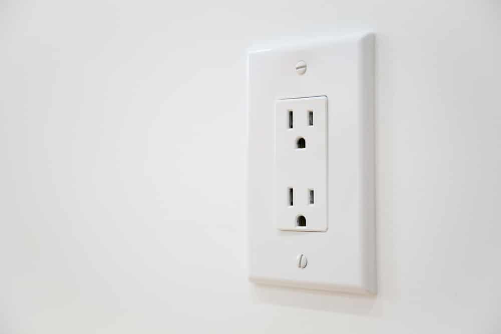 A white electrical outlet with two sockets is mounted on a white wall. The outlet cover, secured with two visible screws, may need electrical outlet troubleshooting if the power outlet is not working but the breaker not tripped. | High 5 Plumbing, Heating & Cooling
