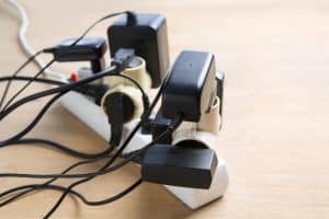 A power strip on a wooden surface with several plugs, adapters, and chargers connected, creating a clutter of cords and an overloaded extension socket, highlighting the importance of electrical cord safety. | High 5 Plumbing, Heating & Cooling