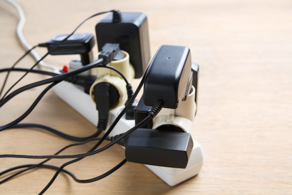 A power strip on a wooden surface with several plugs, adapters, and chargers connected, creating a clutter of cords and an overloaded extension socket, highlighting the importance of electrical cord safety. | High 5 Plumbing, Heating & Cooling